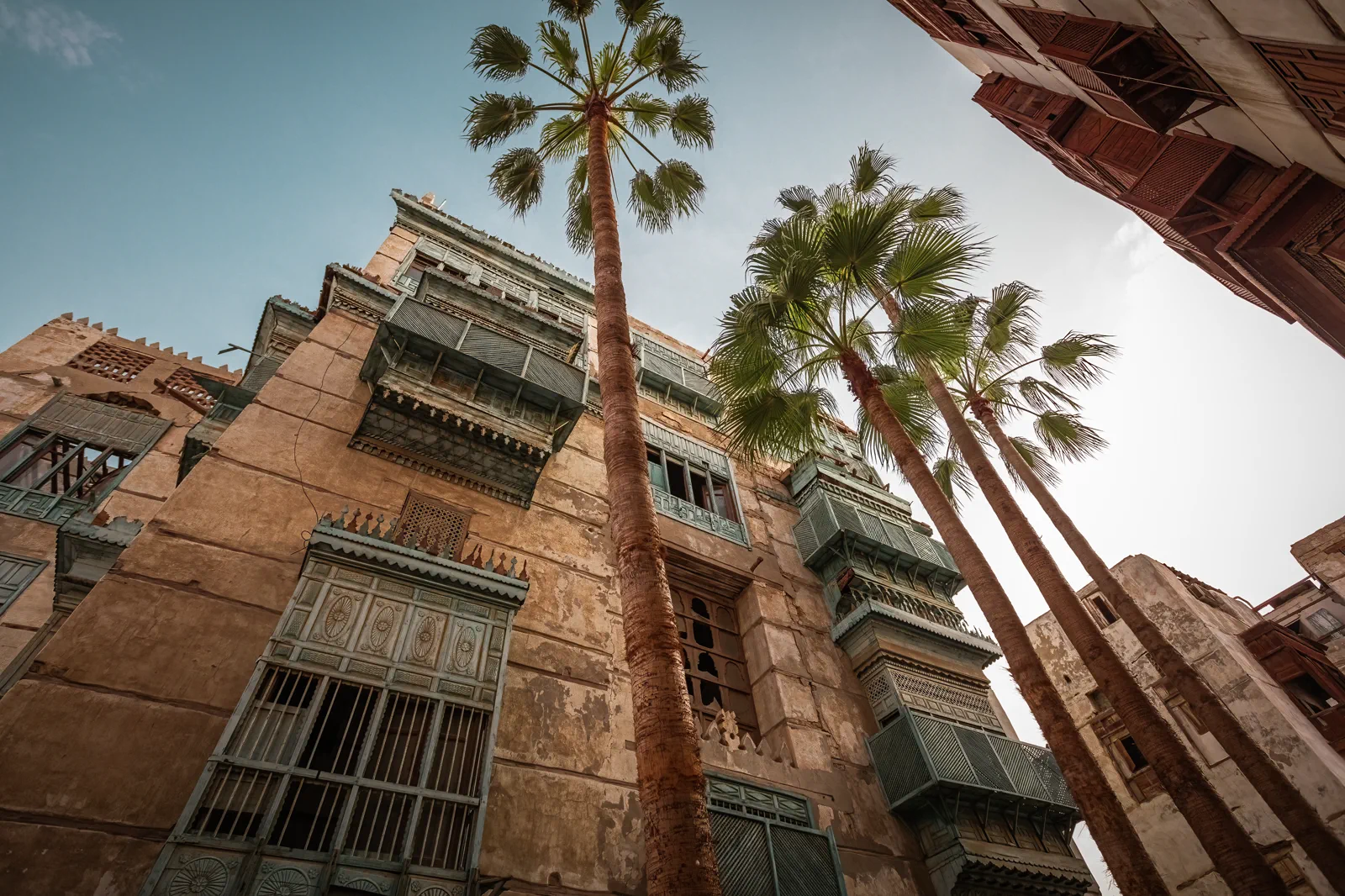 Looking up at Jeddah old-town facade with mashrabiya balconies and palms