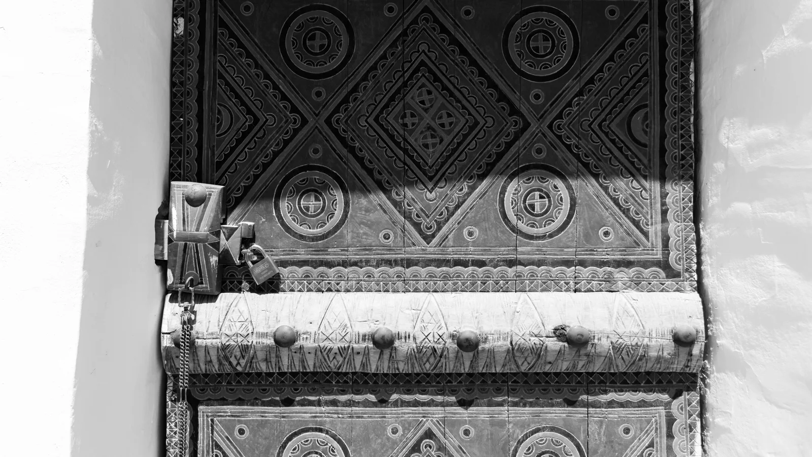Black-and-white close-up of geometric carved door with padlock, Al-Masmak Palace