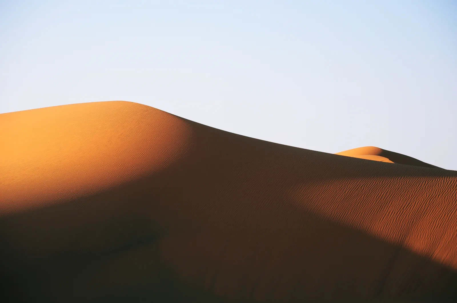 Single amber sand dune under clear blue sky at sunset