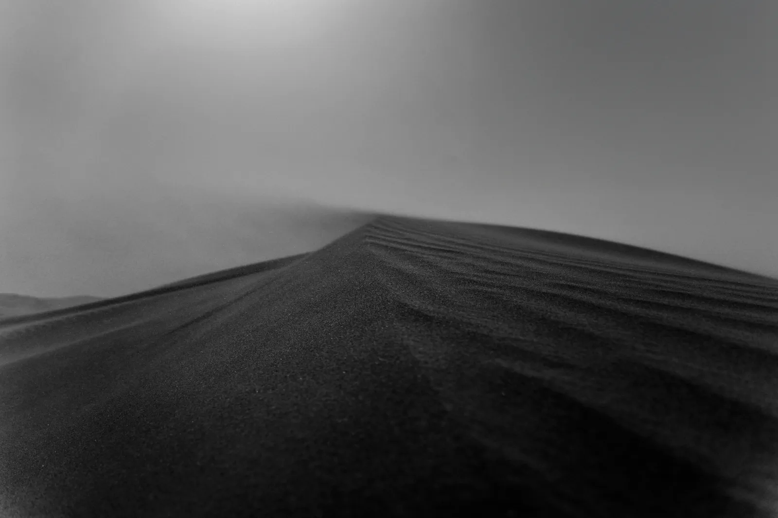 Dark sand dune crest rising through foggy overcast sky