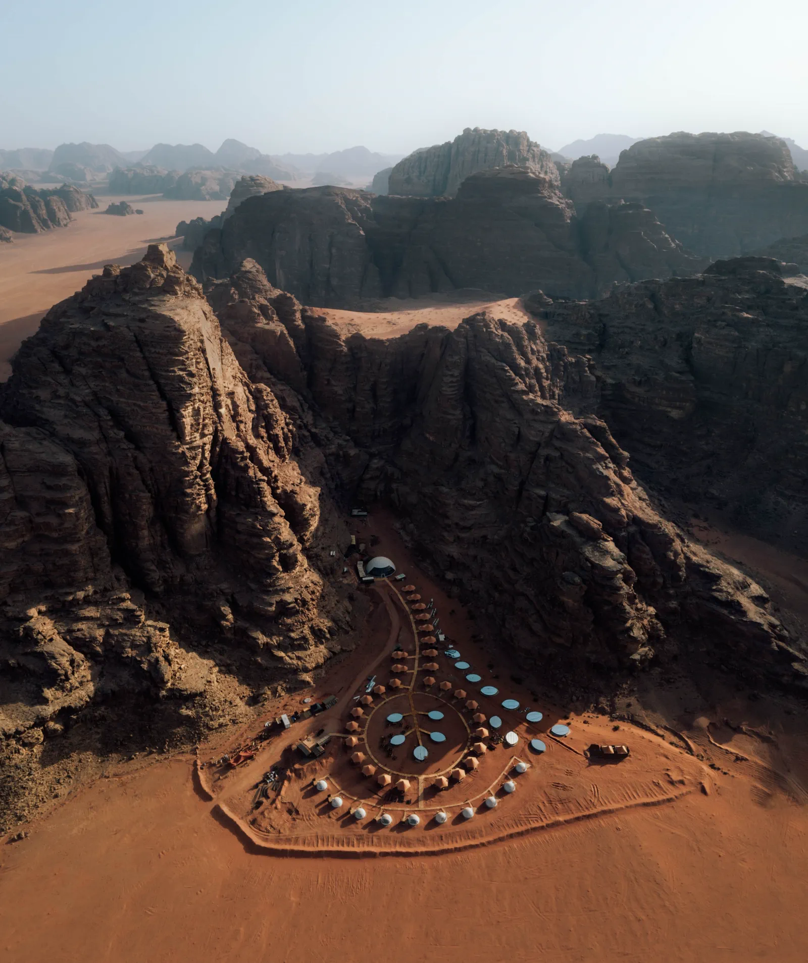 Aerial view of circular desert camp surrounded by red sandstone cliffs
