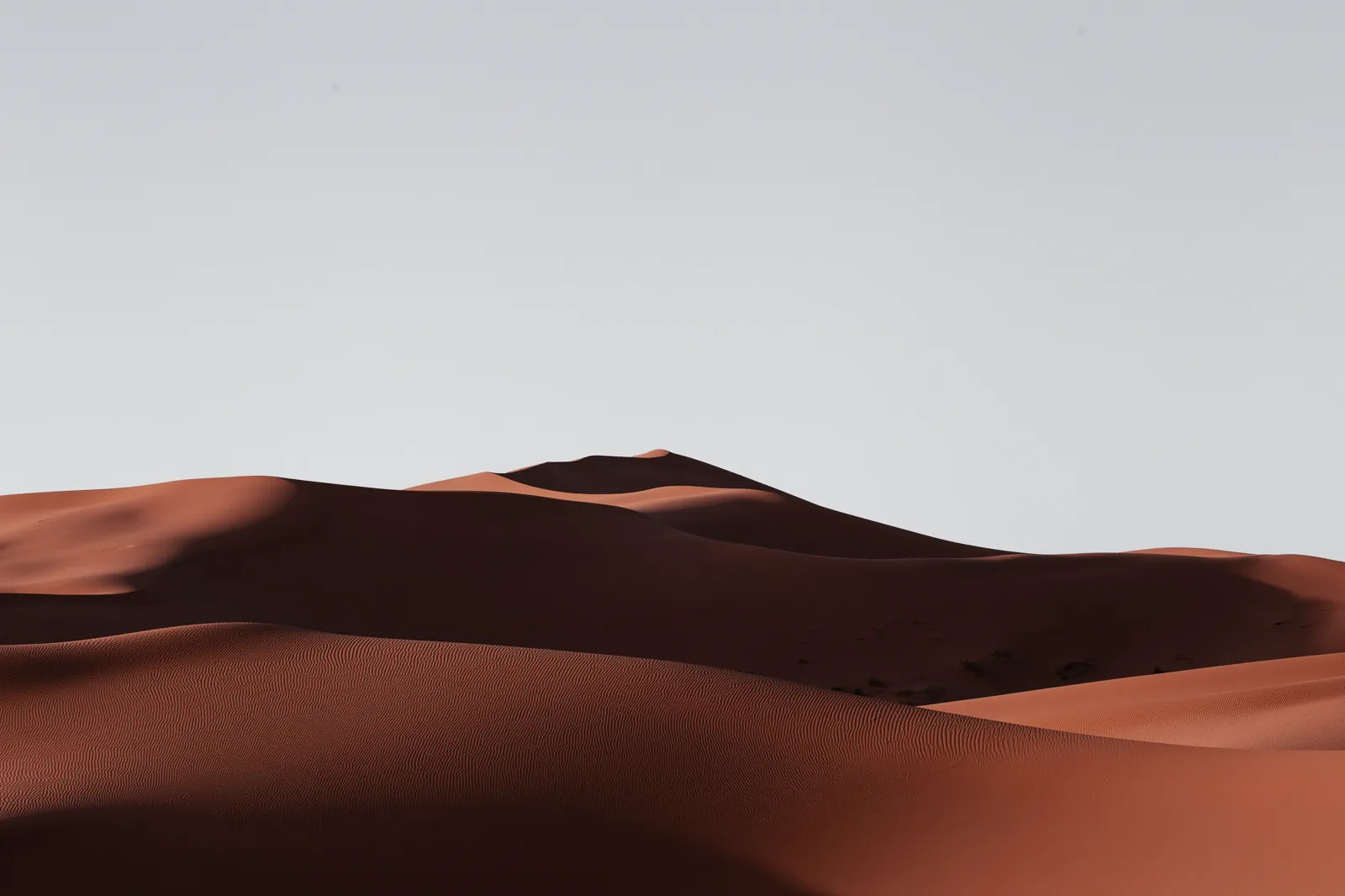 Minimalist deep rust-red sand dunes under a pale overcast sky
