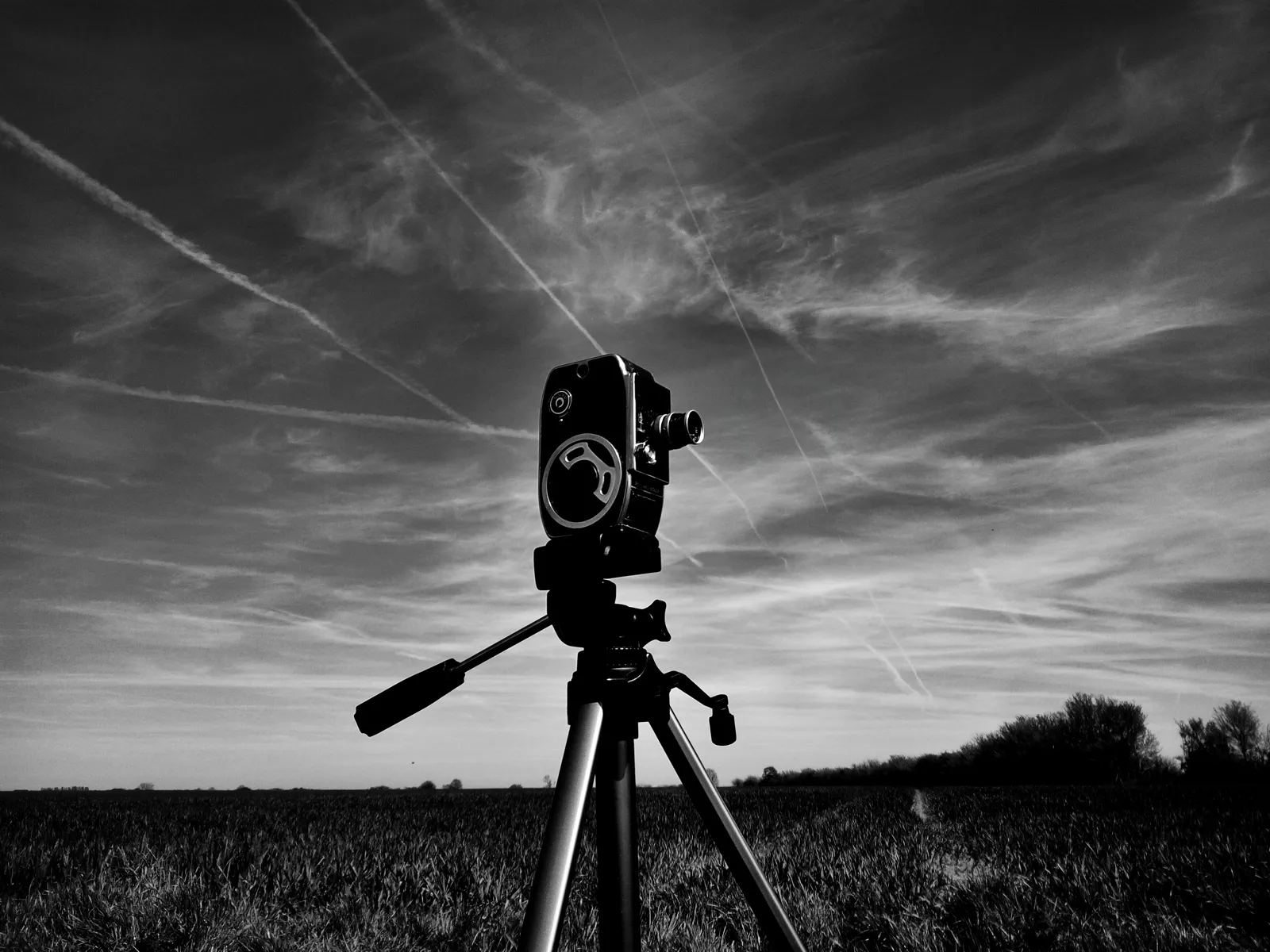Vintage film camera on a tripod against a dramatic sky, black and white